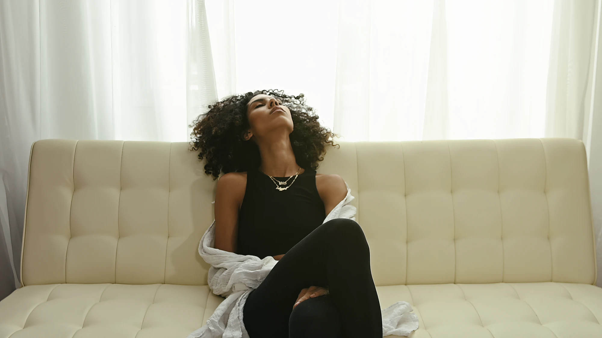 Pj Layne leaning back on a cream sofa, eyes closed, in window light